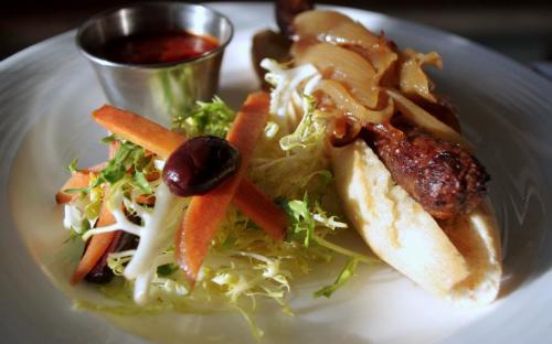 Grilled spicy beef and lamb sausage served on a petite baguette topped with caramelized onions accompanied by a roasted red pepper coulis and carrot, kalamata olive and frisee salad